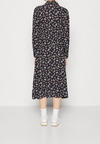 Vestito floreale blu scuro con maniche lunghe e vita stretta. Caratterizzato da motivi floreali bianchi e marroni. Indossato con sneakers bianche e calze a sopracciglio.