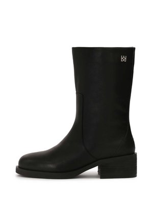 Botte de cheville en cuir noir avec une finition lisse, bout carré et talon bloc. Caractérisée par un subtil détail de logo sur le côté.