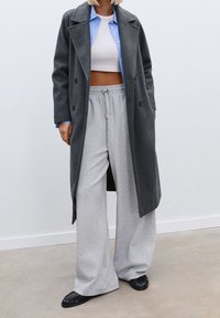 Charcoal gray double-breasted coat layered over a light blue shirt and white crop top, paired with light gray wide-leg pants and black flats.