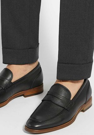 Black leather loafers with a smooth texture, featuring a rounded toe and a decorative strap, paired with dark gray tailored trousers.