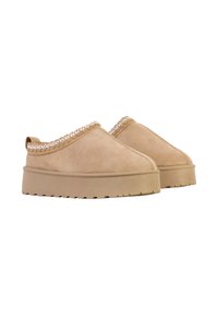Chaussures à enfiler en daim beige avec une semelle épaisse et texturée à plateforme et un accent tressé le long du bord supérieur. Elles présentent un bout rond et une languette arrière.