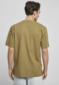 Tricou din bumbac de culoare verde măslin, cu mâneci scurte, croială lejeră și decolteu rotund. Caracteristică o textură netedă și un design simplu.