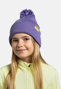 Purple knit beanie with a pom-pom on top, featuring a yellow label. Worn by a child with straight blonde hair, paired with a zip-up yellow jacket.