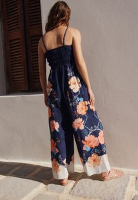 Combineu floral cu corsaj strâns, picioare largi, fundal bleumarin și flori mari portocalii. Accentuate cu detalii albe la tiv.