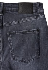 Donkergrijze spijkerbroek met een achterzak en een zwart lederen etiket op de tailleband, met zichtbare stiksels en een gladde textuur.