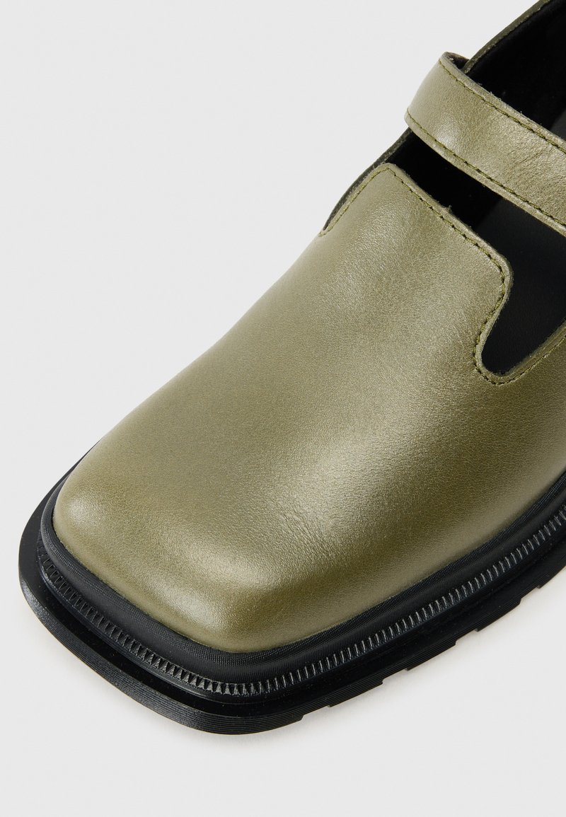 Grüner Lederschuh mit glänzender Oberfläche, runder Zehenpartie und schwarzer Gummisohle. Verfügt über einen Riemen oben für einen sicheren Sitz.