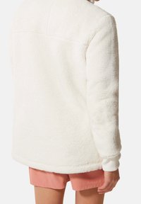 Chaqueta de felpa blanca con un alto cuello, puños acanalados y una textura suave. La vista posterior muestra un diseño sencillo y minimalista.