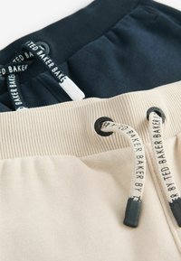 Dos pares de pantalones cortos: uno en azul marino y otro en crema. Cada uno tiene una cinturilla acanalada, cordones con puntas de marca y una textura de tela suave.