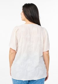 Blusa floreale rosa chiaro realizzata in tessuto strutturato, con maniche a sbuffo corte e una vestibilità morbida, decorata con un sottile motivo di rose in rilievo.