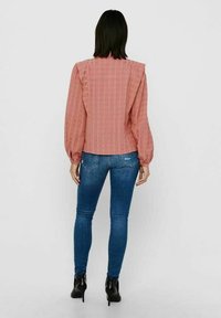 Blusa rosa a trama con maniche a palloncino, caratterizzata da un design a righe; abbinata a jeans skinny blu e stivaletti neri.