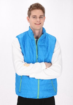 Blauer, pufferartiger Weste mit einem Reißverschluss an der Vorderseite, grünen Akzenten und einem hohen Kragen. Getragen über einem weißen Langarmshirt mit einem orangefarbenen Muster am Ärmel.