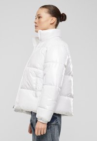 Hvit pufferjakke med en blank overflate, høy krage og quiltet design. Har sidelommer og glidelås-lukking.