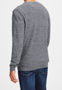 Grauer Strickpullover mit rundem Halsausschnitt, gerippten Bündchen und Saum sowie einer strukturierten Oberfläche. Kombiniert mit dunkelblauen Jeans.