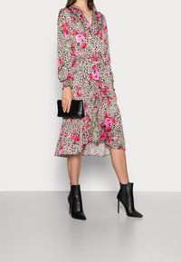 Abito a portafoglio floreale con rose rosa e stampa leopardata. Maniche lunghe, colletto arricciato e gonna a balze. Abbinato a stivaletti neri con tacco e una pochette.