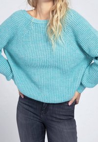 Maglione lavorato a maglia azzurro chiaro con vestibilità ampia, texture a coste, scollatura ampia e maniche lunghe, abbinato a jeans scuri.
