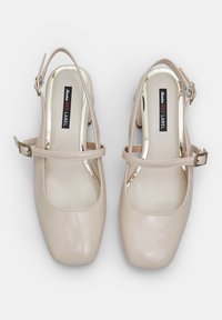 Scarpe slingback in vernice beige con punta quadrata, cinturino alla caviglia e dettagli in metallo dorato. Presentano una soletta imbottita.