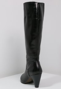 Botte noire en cuir jusqu'au genou avec un talon effilé, texture lisse et détails de couture le long du dos. La base a une finition légèrement texturée.