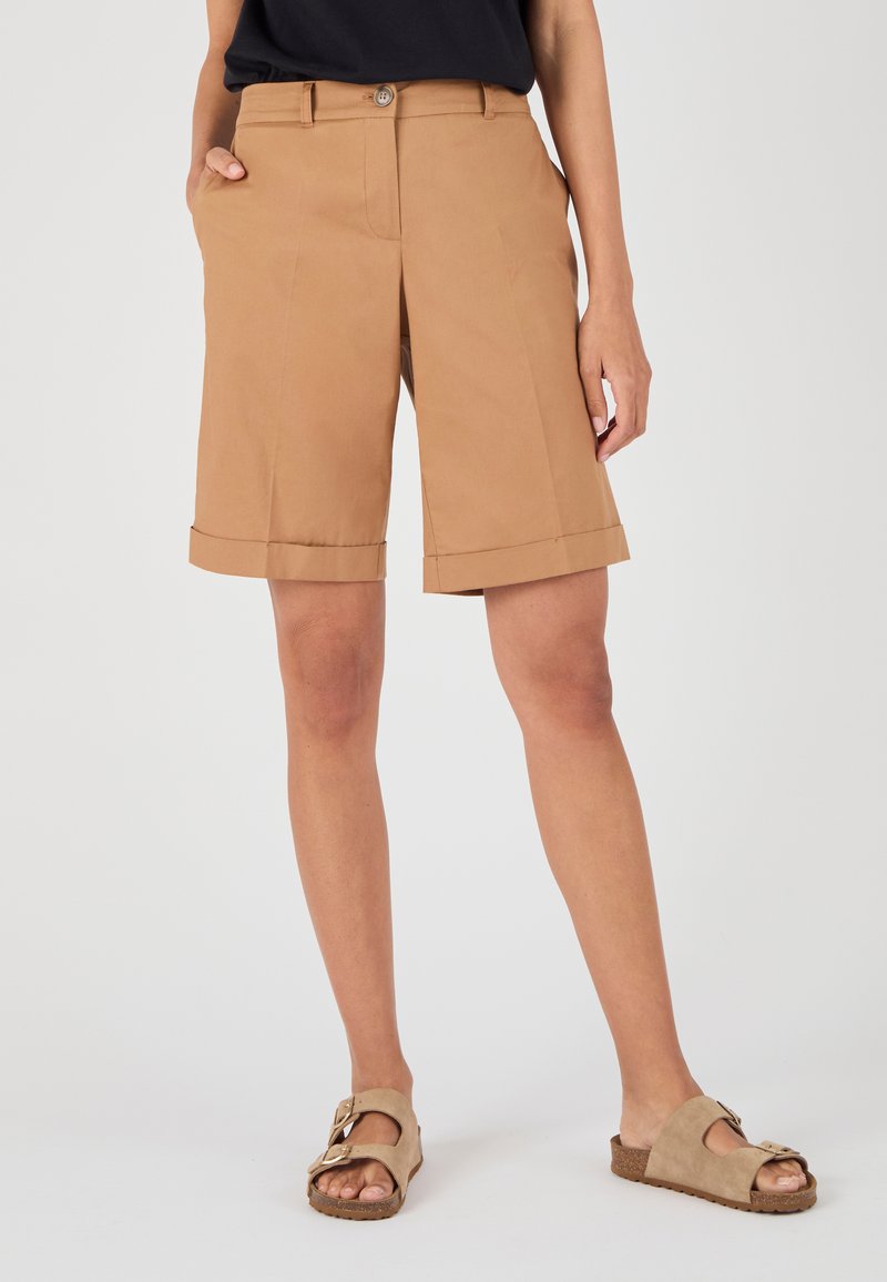 Pantalones cortos de algodón color beige con un corte recto, que presentan un dobladillo doblado y bolsillos laterales. Llevados con sandalias beige claras que tienen un detalle de hebilla.