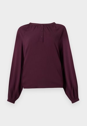 Långärmad blus i plommonlila med rynkad halsringning, treknappsstängning och manschettärmar mot en vit bakgrund.