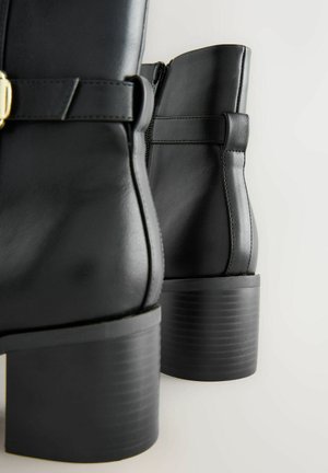 Stivaletti neri in pelle con punta rotonda, tacco spesso, cerniera laterale e una fascia decorativa con una fibbia dorata.