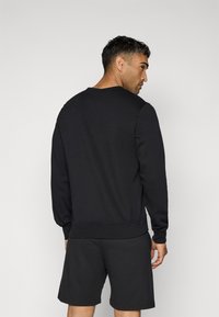 Sweatshirt noir à col ras du cou et poignets côtelés, associé à un short noir assorti. Le tissu semble lisse avec une coupe structurée.