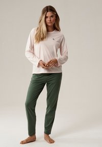 Jasnoróżowa bluzka z długim rękawem z małym zielonym wzorem liścia, w połączeniu z ciemnozielonymi spodniami o tapered. Gładki materiał i luźny krój.