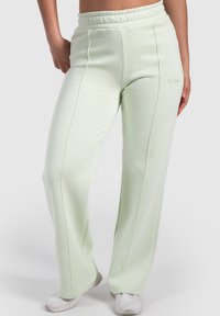 Vaaleanvihreät collegehousut, joissa on joustava vyötärönauha, suorat lahkeet, näkyvät saumat sivuilla ja hillitty logo alhaalla.