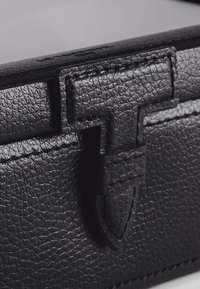 Black textured leather wallet with a T-shaped clasp detail and visible stitching, featuring a sleek, rectangular design.