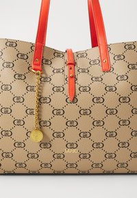 Borsa a spalla color cammello con motivo in rilievo, logo nero e manici in pelle arancione. Presenta un dettaglio con catena d'oro e charm.