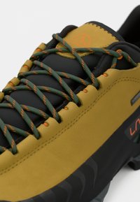 Close-up de um sapato de caminhada amarelo e preto com atacadores verdes e laranja e sola preta robusta.