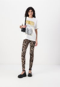 Baltas per didelis marškinėlis su „NEW YORK CITY OF DREAMS“ grafiką, derinamas su prigludusiais leopardų rašto leggingais ir juodais platformos bateliais.