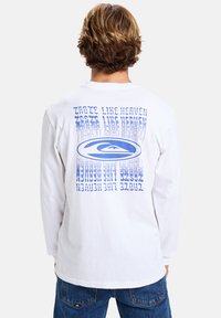 Long-sleeve white T-shirt made of cotton, featuring blue graphic text and logo on the back, casual fit with a round neckline.