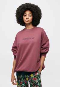 Μπορντό φαρδιά φούτερ με ριμπ λαιμόκοψη και κεντημένο λογότυπο "adidas" στο κέντρο, σε συνδυασμό με παντελόνι με λουλουδάτο μοτίβο.