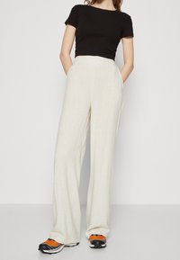 Pantalones anchos de lino blanco con una cintura alta, combinados con una camiseta negra ajustada y zapatillas deportivas multicolores. Textura suave y tejido transpirable.