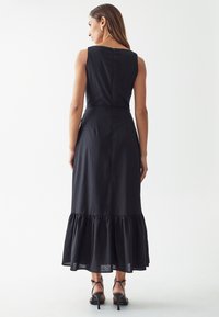 Black sleeveless dress with a fitted bodice and flared ruffled hem. Made of soft fabric with a subtle sheen, featuring a back zipper closure.