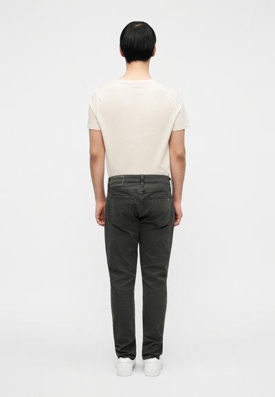 Αντρικό σύνολο που περιλαμβάνει απλό κρεμ t-shirt και στενά σκούρα πράσινα παντελόνια, συνδυασμένο με λευκά αθλητικά παπούτσια. Μινιμαλιστικός σχεδιασμός και ουδέτεροι τόνοι.