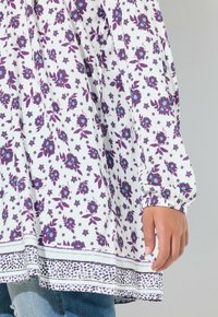 Blusa bianca con motivo floreale viola, polsini elastici arricciati e design con orlo a strati con rifiniture a contrasto e piccoli puntini.