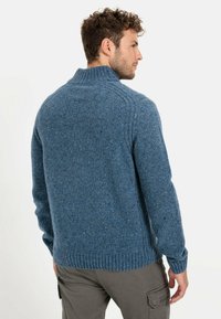 Blauer Wollpullover mit hohem Kragen, gerippten Bündchen und Saum, der ein strukturiertes Strickdesign mit subtilen Farbtupfern aufweist.