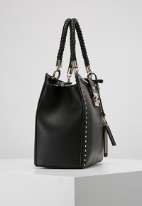 Sac à main en cuir noir avec des poignées tressées, quincaillerie en argent et des clous décoratifs sur un côté. Forme structurée avec une fermeture éclair.