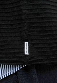 Fekete bordázott pulóver szőtt textúrával. Jellemzője egy fehér címke, amin az "JACK & JONES" felirat található. Alatta egy csíkozott anyag található tengerészkék és fehér színben.