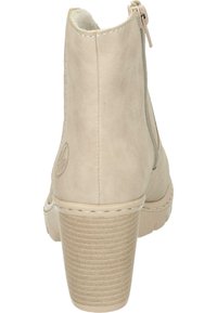 Bottine en suède beige avec un talon texturé épais, fermeture éclair sur le côté et un détail de couture subtil. Présente un logo sur le talon extérieur.