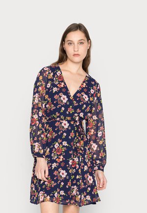 Vestido floral envolvente com fundo azul-marinho, mangas longas translúcidas, decote em V profundo e cintura com laço. O padrão inclui flores de variadas cores.