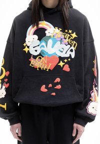 Sudadera de forro polar negra con diseños de apliqué coloridos, que incluyen un arcoíris, nubes, corazones y el texto: "El cielo en la Tierra". Incluye un bolsillo frontal.