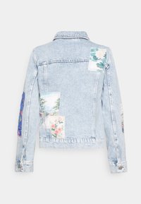 Light blue denim jacket with varied floral fabric patches. Features a classic collar, buttoned cuffs, and a slightly faded texture.