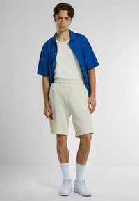Blå kortærmet skjorte, hvid tanktop, cremefarvede ribbede shorts, hvide sneakers og stribede sokker. Enkel, afslappet outfit med kontrasterende farver.
