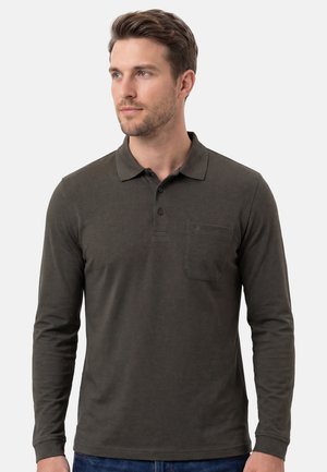 Mann trägt dunkelgraues langärmliges Poloshirt mit Brusttasche, schaut leicht nach links vor einem schlichten hellen Hintergrund.