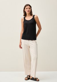 Top a manica scoperta nera con rouches sulle spalle, abbinato a pantaloni larghi di colore chiaro e sandali neri con fibbie decorative.
