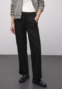 Schwarze Jogginghosen aus weichem Stoff mit Tunnelzug am Bund, Seitentaschen und lockerer Passform, ergänzt durch elegante schwarze Stiefeletten.