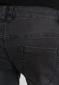 Jeans de ganga pretos com uma textura suave, corte reto e bolso traseiro com detalhes de costura.
