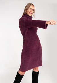 Lila, fuzzy Strickkleid mit hohem Kragen und langen Ärmeln, das eine figurbetonte Silhouette und einen asymmetrischen Saum aufweist.